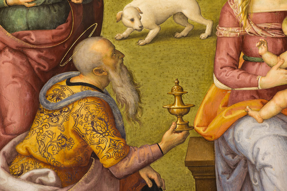 A detail of the fresco. One of the Wise Men, richly clad and with a halo on his head, kneels beside the Baby Jesus and hands him a golden box.