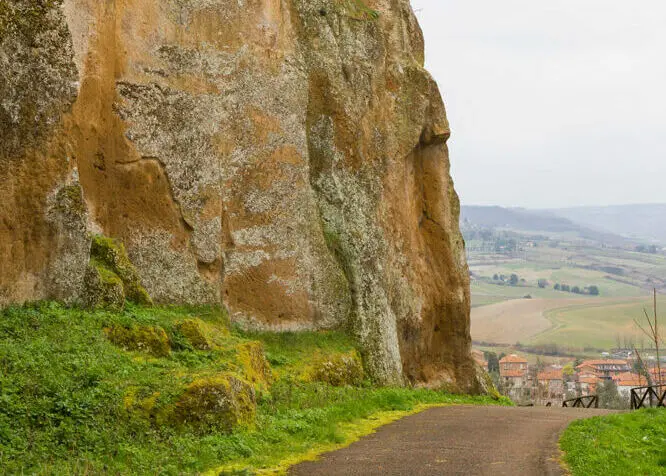 Tratto del sentiero dell’Anello della Rupe, in terra battuta. A sinistra si erge la rupe, in tufo dal caratteristico colore rossastro, e sullo sfondo le campagne orvietane.