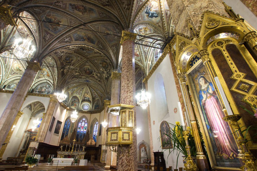 Vista dell'interno della Cattedrale di San Lorenzo con vista della Madonna delle Grazie sulla destra. La sinistra dell'immagine è occupata dalla navata centrale della chiesa che mostra le colonne e le volte affrescate.