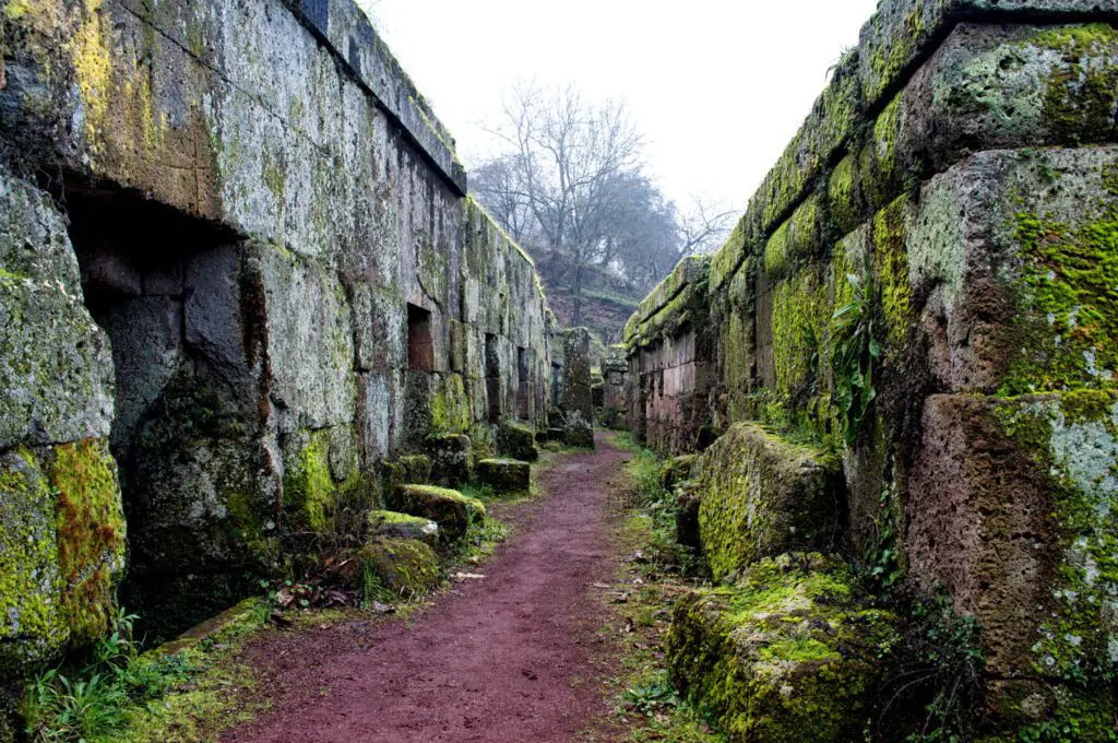 Veduta leggermente scorciata di un tratto di percorso della Necropoli del Crocifisso. Al centro il percorso in terra battuta, ai lati le tombe in pietra.