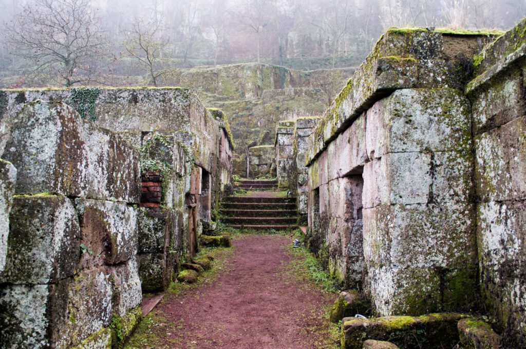 Veduta di un tratto di percorso della Necropoli del Crocifisso. Il percorso è in terra battuta, di fronte una breve scalinata, ai lati le tombe in pietra.