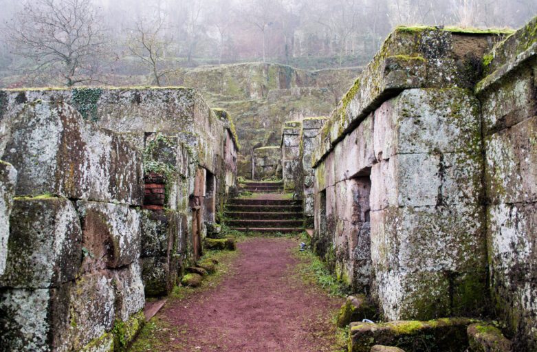 Veduta di un tratto di percorso della Necropoli del Crocifisso. Il percorso è in terra battuta, di fronte una breve scalinata, ai lati le tombe in pietra.