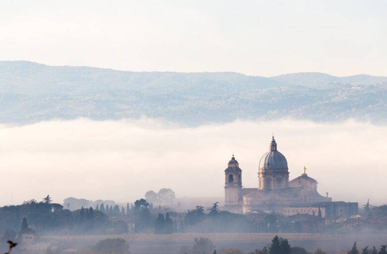 Vista panoramica di Santa Maria degli Angeli. La struttura della chiesa, con il suo cupolone, si erge dalle campagne umbre e spicca dalla nebbia della piana in cui si trova.