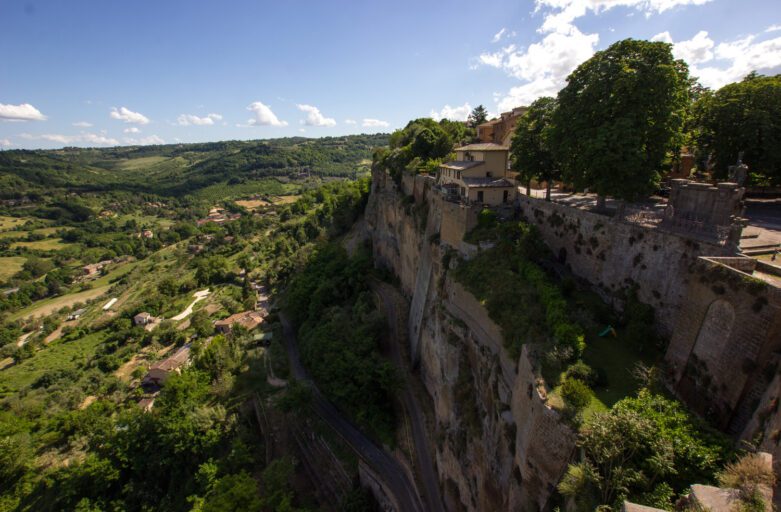 Vista dall'alto di un tratto del percorso dell'Anello della Rupe. Dalla Rocca Albornoz, guardando oltre ai muri che danno sullo strapiombo della Rupe, è possibile vedere un tratto del percorso di trekking che ad anello circumnaviga Orvieto. Sulla destra la rupe, che si tuffa verticalmente nel verde che ricomprendi tutta la parte sinistra dell'immagine.