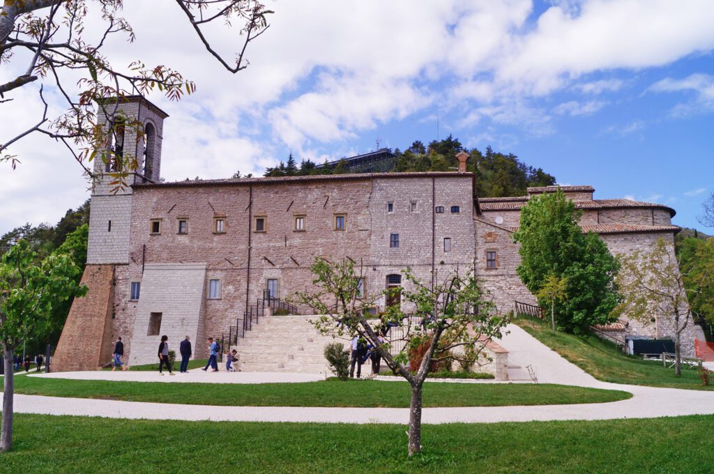 Vista della Basilica di Sant’Ubaldo, a cui piedi si trova un prato con una stradina che porta alla grande scalinata e all’ingresso.