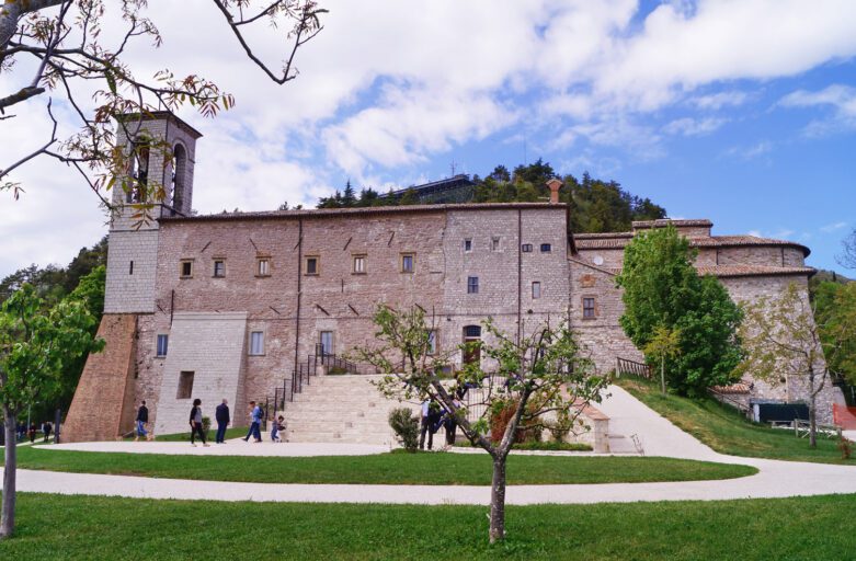 Vista della Basilica di Sant’Ubaldo, a cui piedi si trova un prato con una stradina che porta alla grande scalinata e all’ingresso.