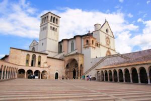 Vista della Basilica Inferiore di Assisi. In primo piano la piazza, circondata di portici, e al centro, sullo sfondo, il complesso della basilica.