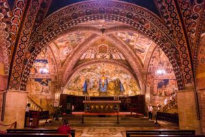 Vista dell'altare nella basilica inferiore. Le volte totalmente affrescate sono illuminate da lampadari in quanto non vi sono aperture per far entrare lice naturale.