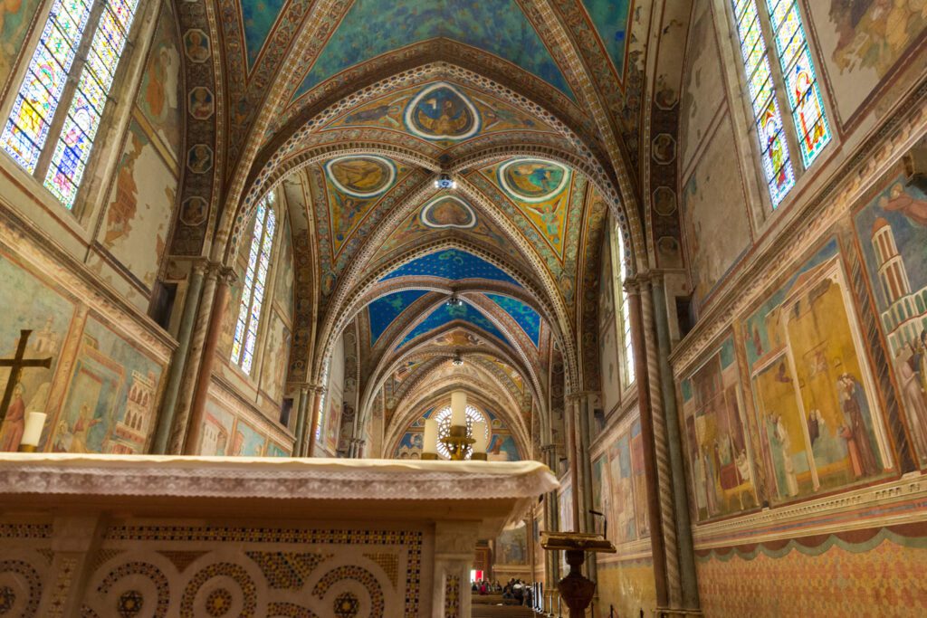 Vista della Basilica Superiore con lo sguardo rivolto verso la controfacciata. In primo piano la porzione superiore dell'altare e sullo sfondo la navata unica interamente affrescata.