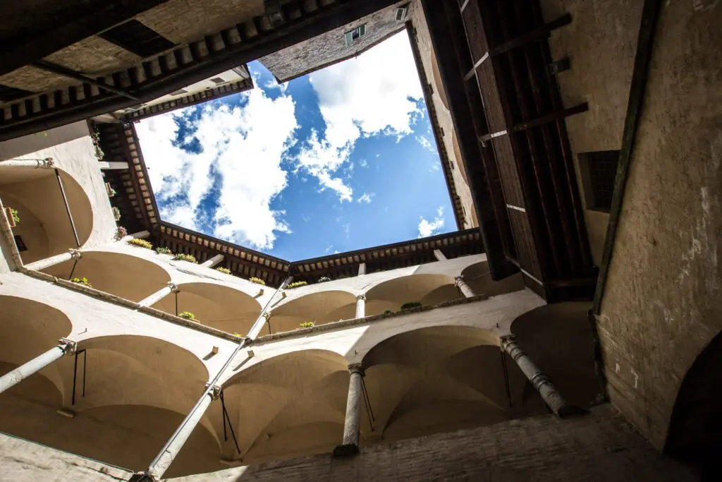 Sguardo verso l'alto dal chiostro inferiore dell'isola di San Lorenzo. Dei due livelli del chiostro sono visibili solo gli archi che si affacciano sul chiostro. Un pezzo di cielo con qualche nuvola è al centro dell'immagine.