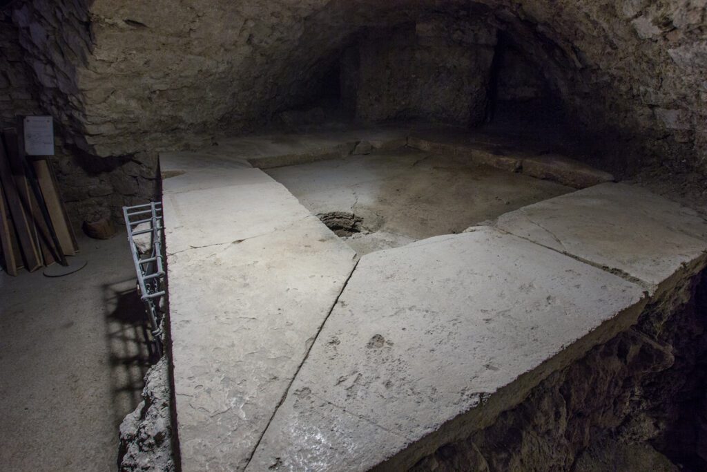Vista dell'impluvium della domus romana. Rialzata dall'attuale piano del calpestio si trova l'impluvium, cioè il luogo adibito alla raccolta dell'acqua piovana. Questo consiste in una cornice di roccia squadrata che delimita una piccola vasca con un buco nel quale l'acqua confluiva.