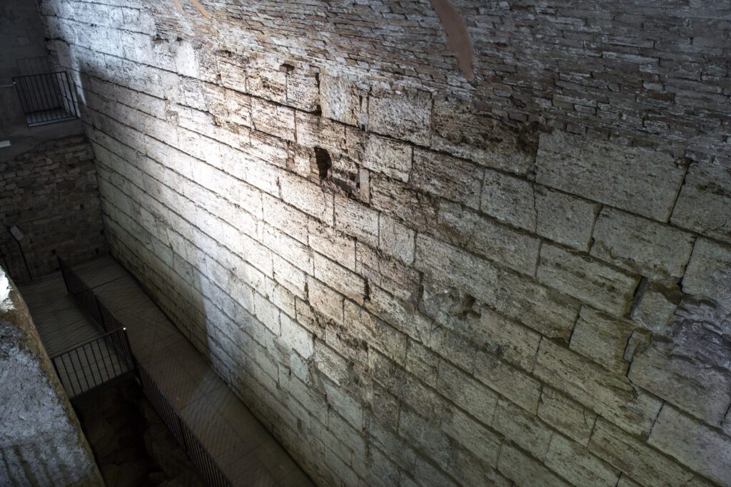 Vista dall'alto del muro etrusco di terrazzamento che contiene la terra della collina e sorregge l'attuale piazza di Perugia. Il muro è realizzato con grandi conci squadrati di travertino, messi in opera senza leganti. In basso il camminamento che fiancheggia il muro, in alto la muratura in mattoni costruita successivamente.