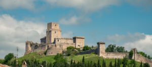 Vista della Rocca Maggiore da Assisi. L'imponente costruzione svetta sul monte ergendosi sui verdi boschi che la circondano.