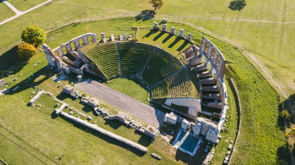 Vista aerea del Teatro Romano. È ben visibile la forma a semicerchio della cavea, delimitata all’esterno dagli archi in muratura, che guarda all’orchestra e al proscenio.