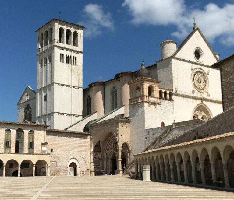 Vista della Basilica di San Francesco dalla piazza sottostante. La piazza è vuota, il cielo azzurro.