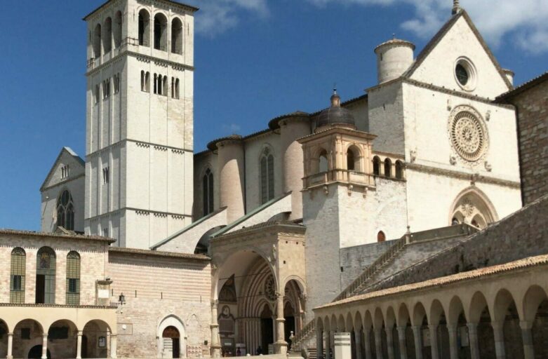 Vista della Basilica di San Francesco dalla piazza sottostante. La piazza è vuota, il cielo azzurro.