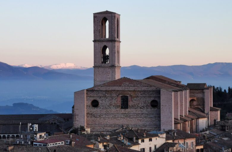 Vista in lontananza dell'imponente Basilica di San Domenico. La struttura svetta enormemente sull'abitato, con il suo campanile che si protende verso il cielo. Sullo sfondo il paesaggio montano visibile da Perugia.