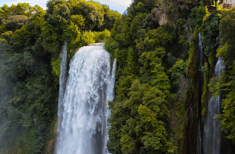 Vista della parte apicale delle Cascate delle Marmore, a Terni. L’acqua scende velocemente da pendici coperte di fitto bosco verdissimo.