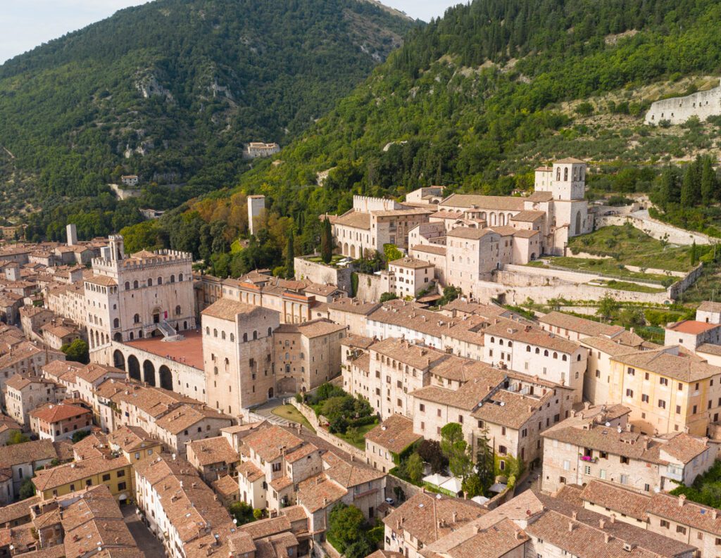 Gubbio: vista aerea della città arroccata sulle verdi pendici del monte coperte di boschi. Spiccano Piazza Grande e il Palazzo dei Consoli.