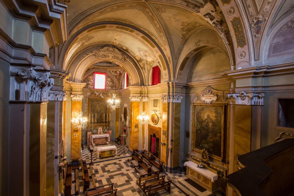 Vista dall'alto dell'interno della chiesa collegata all'Oratorio di Santa Maria dei Bianchi. Ad altezza occhi i capitelli delle colonne aggettate ai muri. In basso il pavimento decorato, sul fondo l'abside della chiesa.
