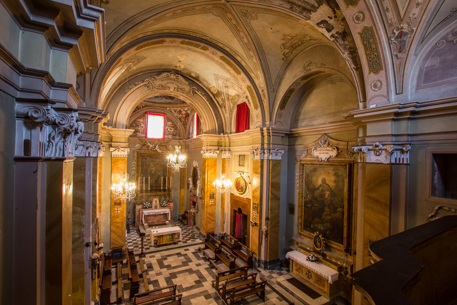 Vista dall'alto dell'interno della chiesa collegata all'Oratorio di Santa Maria dei Bianchi. Ad altezza occhi i capitelli delle colonne aggettate ai muri. In basso il pavimento decorato, sul fondo l'abside della chiesa.