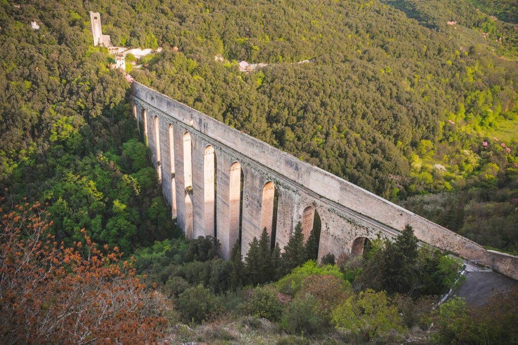 Vista aerea scorciata del Ponte delle Torri. Il ponte è visibile in tutta la sua lunghezza dalla pendice di Colle Sant'Elia fino al fortilizio posto su Monteluco. Il fortilizio emerge dal fitto bosco.