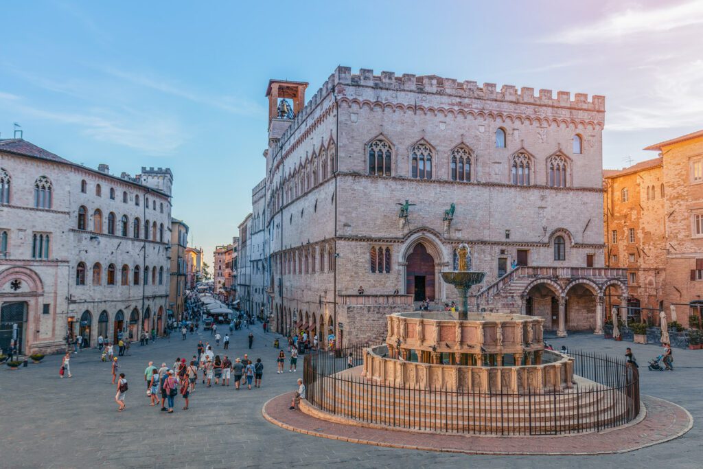 Vista della Fontana Maggiore dando le spalle alla Cattedrale.Sulla destra campeggia la fontana, il cui sfondo è la facciata del palazzo dei priori. Sulla sinistra si apre corso vannucci, sfruttabile a perdita d'occhio nella sua lunghezza.