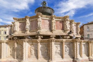 Vista ravvicinata delle due vasche in marmo rosa e bianco. Sulla vasca inferiore sono visibili le formelle con bassorilievi, mentre nella superiore le sculture. Più in alto emerge la vasca con le statue in bronzo.
