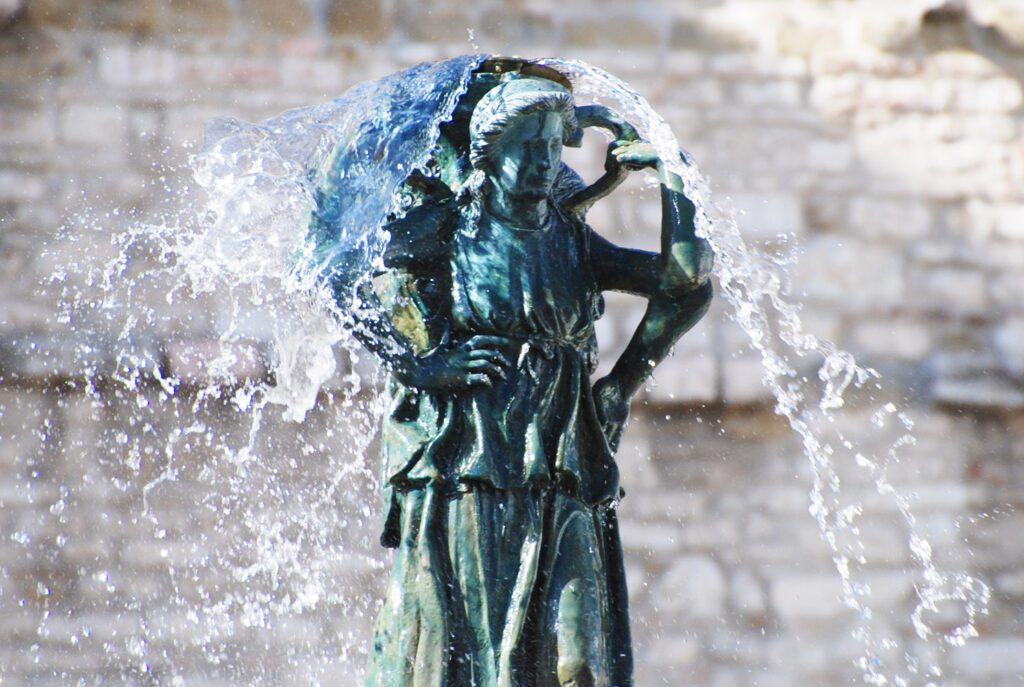 Vista ravvicinata della scultura in bronzo delle tre donne che, dandosi le spalle vicendevolmente, sorreggono sopra le loro teste un'anfora dalla quale sgorga l'acqua della fontana maggiore.