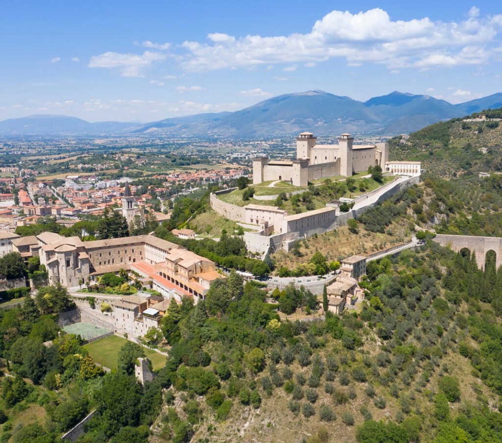 Spoleto: vista aerea della città, con Rocca Albornoz in cima alla collina e Ponte delle Torri immersa nel verde sulla destra.