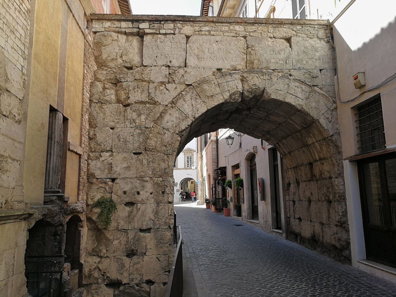 Vista ravvicinata dell'Arco di Druso a Spoleto. L'arco, sulla sinistra, è appoggiato a un edificio recente.