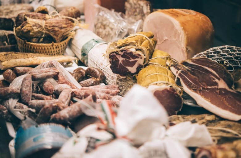 Vista di un bancone imbandito di salumi e affettati. Capocollo, salsicce secche, prosciutto e altri insaccati riempiono l'immagine.