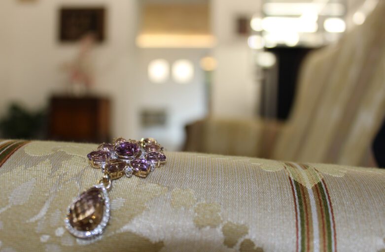 In primo piano un elaborato collier con pietre preziose violacee incastonate in una struttura di oro. Sullo sfondo parte dello showroom della gioielleria.