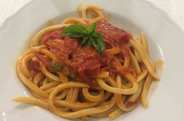 Inquadratura dall’alto di un piatto di umbricelli conditi con passata di pomodoro e una foglia di basilico a decorazione sopra.