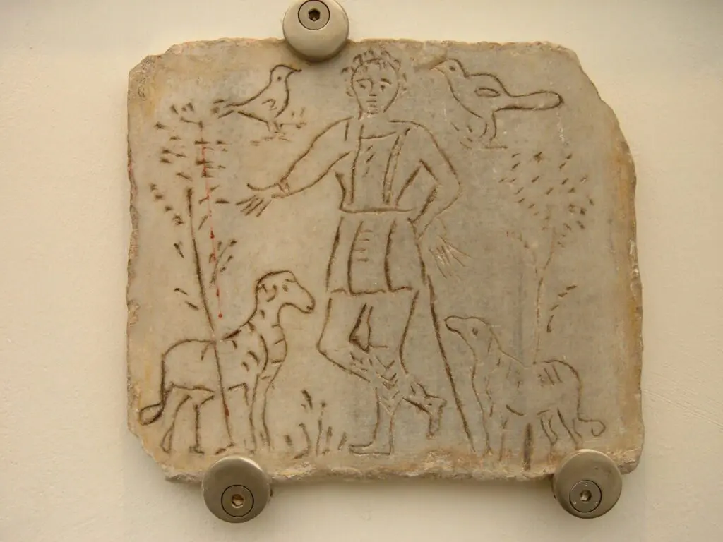 pietra funeraria risalente al periodo dell’antica Roma dove un’incisione raffigura un pastore con due pecore al suo lato destro e sinistro. Sono raffigurate anche delle graminacee a simboleggiare gli animali al pascolo e due uccelli che volano in alto, accanto alla testa del pastore. La pietra si trova al Museo Nazionale Romano, nell’area delle Terme di Diocleziano.