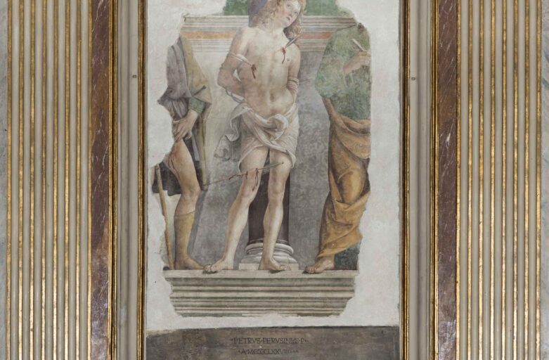 Overall view of the fresco. In the centre, there is Saint Sebastian tied to a column, his head and gaze turned upwards and his body is pierced by three arrows, two on his chest and one on his right leg. He is completely naked, except from a cloth covering his hips. On the left, there is part of a human figure showing a bleeding wound on the left inner thigh (presumably St. Roch) wearing a short tunic and another one on the right wearing a long tunic holding a key in his right hand (probably St. Peter).