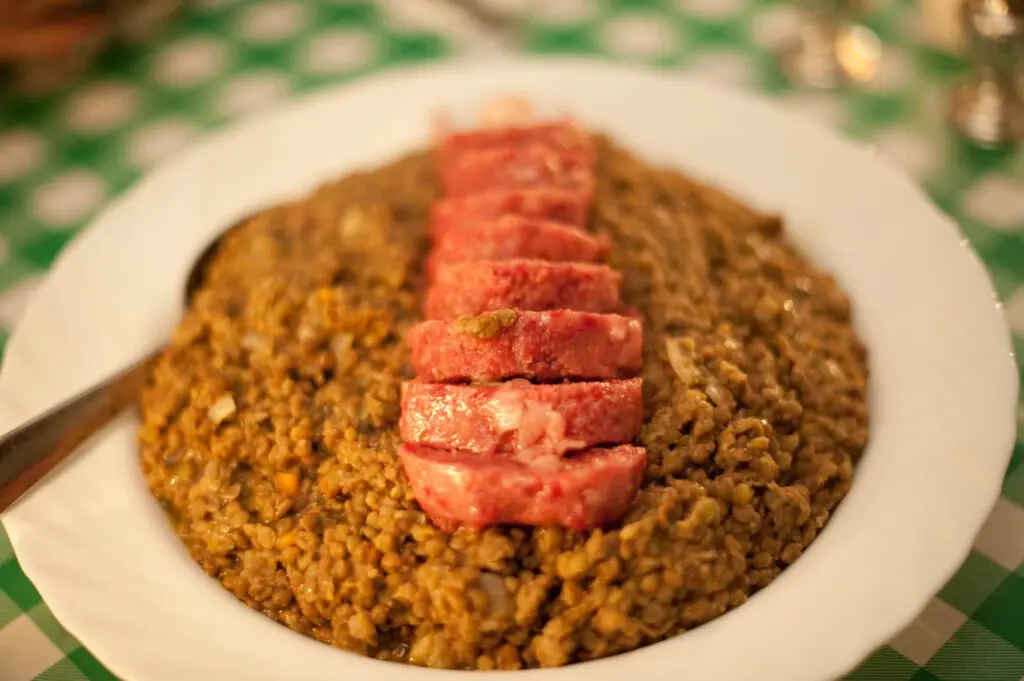 inquadratura su un piatto di fette di zampone adagiate su un piatto di lenticchie cotte.