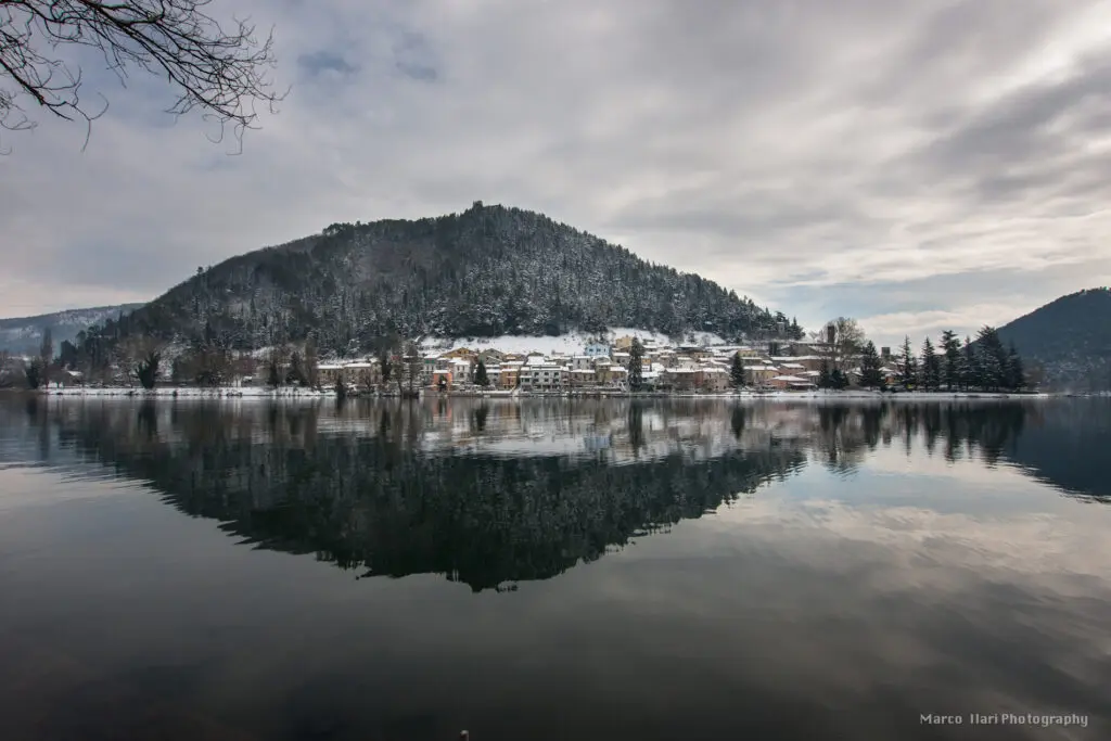 Foto del Lago di Piediluco scattata alle prime luci dell’alba. Il paesaggio lacustre, circondato dalle montagne, è ricoperto di nebbia e una leggera luce del mattino si riflette con diverse sfumature sulla nebbia.