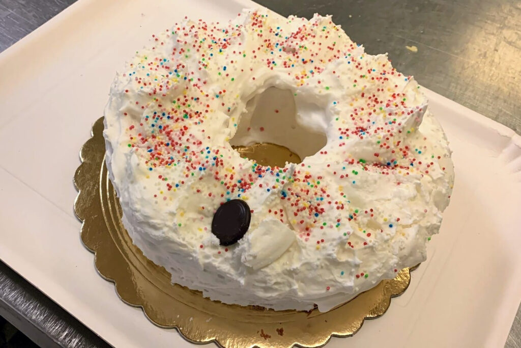 Photo from above of ciaramicola, a typical Easter cake baked in Perugia. It has the shape of a donut with a central hole, covered with white icing similar to a meringue with coloured sprinkles.