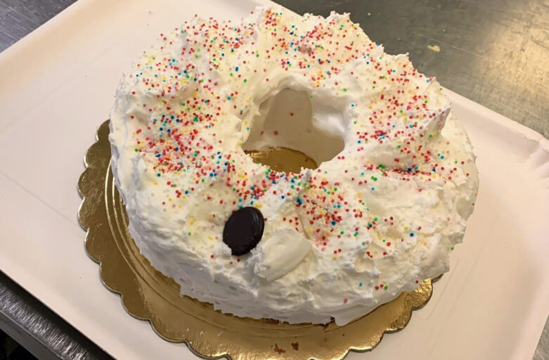 Photo from above of ciaramicola, a typical Easter cake baked in Perugia. It has the shape of a donut with a central hole, covered with white icing similar to a meringue with coloured sprinkles.
